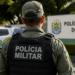 Policial da Polícia Militar do Piauí visto de costas em área externa, com viatura ao fundo.