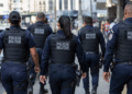 Grupo de policiais militares do Rio de Janeiro caminhando de costas em patrulhamento urbano.
