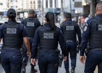 Grupo de policiais militares do Rio de Janeiro caminhando de costas em patrulhamento urbano.