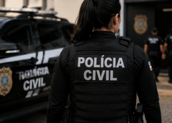 Policial civil de costas com viatura em operação.