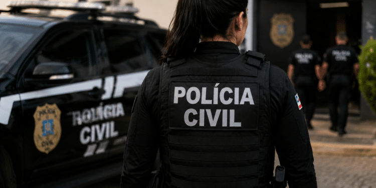 Policial civil de costas com viatura em operação.