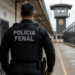 Agente da Polícia Penal de costas em ambiente prisional durante atuação de segurança.