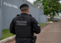 Policial penal de costas em frente a unidade prisional.