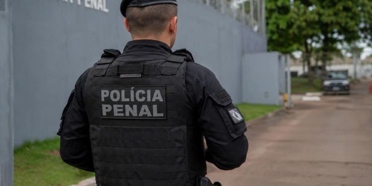 Policial penal de costas em frente a unidade prisional.