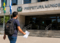 Candidato caminha em direção à Prefeitura Municipal segurando documento de concurso público.