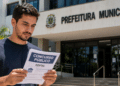 Homem lendo edital de concurso público em frente à Prefeitura Municipal em dia ensolarado.