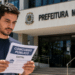 Homem lendo edital de concurso público em frente à Prefeitura Municipal em dia ensolarado.