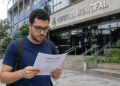Homem lê edital de concurso público em frente à Prefeitura Municipal.