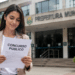 Mulher segurando edital de concurso público em frente ao prédio da Prefeitura Municipal.