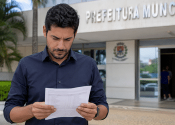 Candidato lê documento de concurso público em frente à Prefeitura Municipal.
