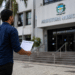 Homem caminhando em direção à prefeitura municipal segurando documento de concurso público.