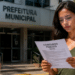 Mulher lê edital de concurso público em frente à prefeitura municipal.