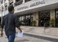 Homem caminhando em direção à prefeitura municipal segurando documento de concurso público.