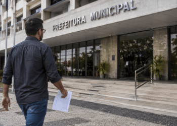 Homem caminhando em direção à prefeitura municipal segurando documento de concurso público.
