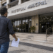 Homem caminhando em direção à prefeitura municipal segurando documento de concurso público.