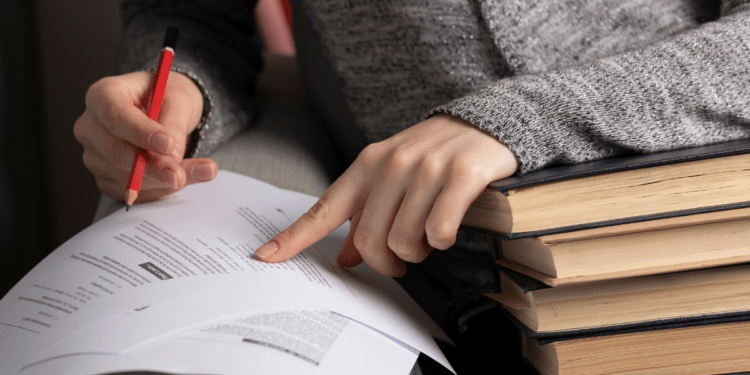 Pessoa consultando documento de concurso público com livros ao lado, representando estudo para seleção da Prefeitura de Itupeva.