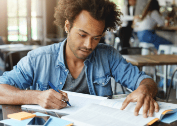 Jovem estudando em mesa com livros e caderno aberto, representando preparação para concurso da Câmara de Rio das Ostras e Prefeitura de Alto do Rio Doce.
