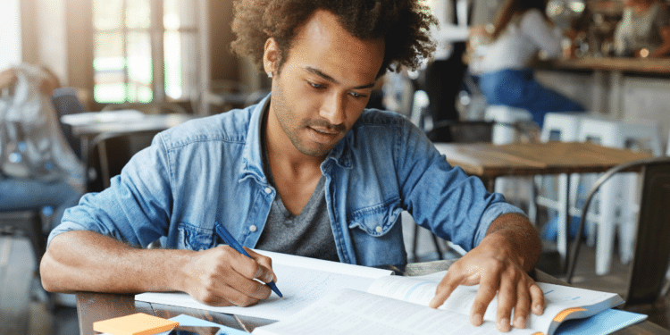 Jovem estudando em mesa com livros e caderno aberto, representando preparação para concurso da Câmara de Rio das Ostras e Prefeitura de Alto do Rio Doce.