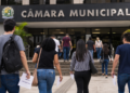 Pessoas caminham em direção à Câmara Municipal segurando documentos de concurso público.