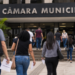 Pessoas caminham em direção à Câmara Municipal segurando documentos de concurso público.