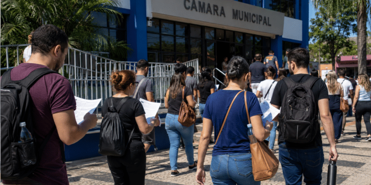 Candidatos com documentos de concurso caminham em direção a uma Câmara Municipal.