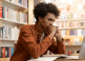 Jovem estudando em biblioteca com notebook e livros, representando candidatos interessados nos concursos da CGU e da ANPD autorizados pelo MGI.