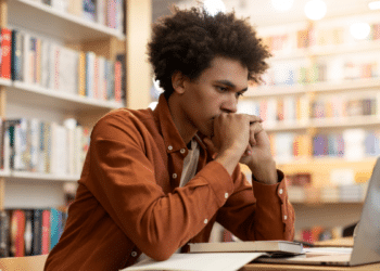 Jovem estudando em biblioteca com notebook e livros, representando candidatos interessados nos concursos da CGU e da ANPD autorizados pelo MGI.