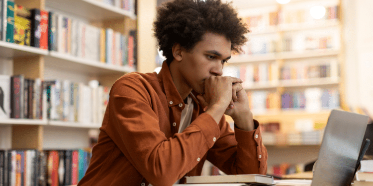 Jovem estudando em biblioteca com notebook e livros, representando candidatos interessados nos concursos da CGU e da ANPD autorizados pelo MGI.