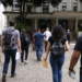 Pessoas com mochilas e documentos caminham em direção a prédio público para participar de seleções municipais.