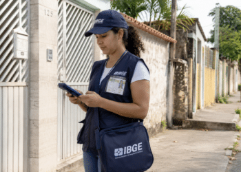 Profissional do IBGE em trabalho de campo durante coleta de informações em rua residencial.