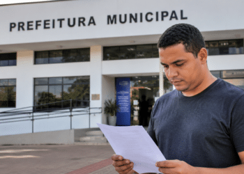 Homem analisa documento de concurso público em frente à prefeitura municipal.