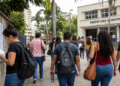 Candidatos caminham em direção à prefeitura municipal com editais e documentos de concurso público em mãos.