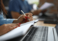Pessoa fazendo anotações em caderno ao lado de um notebook, representando concursos públicos em SP com inscrições abertas..