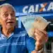 Idoso brasileiro segura cédulas de real em frente a uma agência da Caixa, representando a consulta aos depósitos do INSS de até R$ 8.475,55.