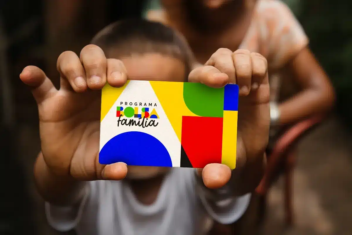 Criança segura cartão do Bolsa Família, representando o processo de consulta da data de pagamento e movimentação do benefício.