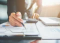 Profissional analisando documentos e gráficos financeiros em ambiente de escritório, representando planejamento para abertura de negócio contábil.