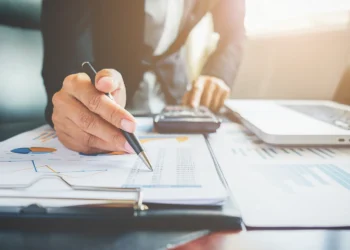 Profissional analisando documentos e gráficos financeiros em ambiente de escritório, representando planejamento para abertura de negócio contábil.