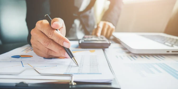 Profissional analisando documentos e gráficos financeiros em ambiente de escritório, representando planejamento para abertura de negócio contábil.