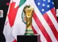 Troféu da Copa do Mundo da FIFA 2026 em destaque com bandeiras dos países-sede ao fundo durante fase eliminatória.