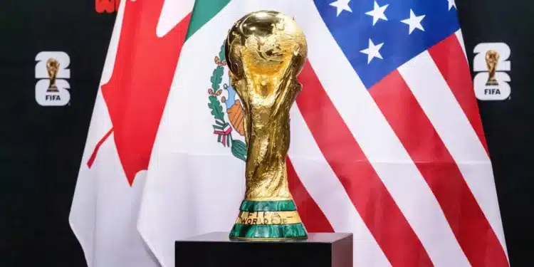 Troféu da Copa do Mundo da FIFA 2026 em destaque com bandeiras dos países-sede ao fundo durante fase eliminatória.