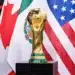 Troféu da Copa do Mundo da FIFA 2026 em destaque com bandeiras dos países-sede ao fundo durante fase eliminatória.