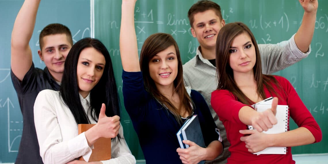 Grupo de estudantes comemora com os braços erguidos diante de um quadro com fórmulas