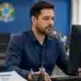 Corretor de redação analisa informações no computador enquanto uma pasta do Enem sobre redação e notas aparece sobre a mesa.