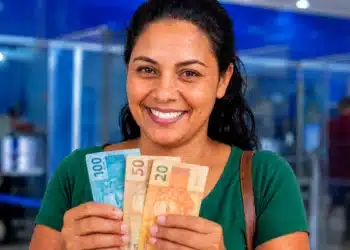 Mulher segurando cédulas em agência bancária, representando o calendário de pagamentos e os adicionais do Bolsa Família em junho de 2026.