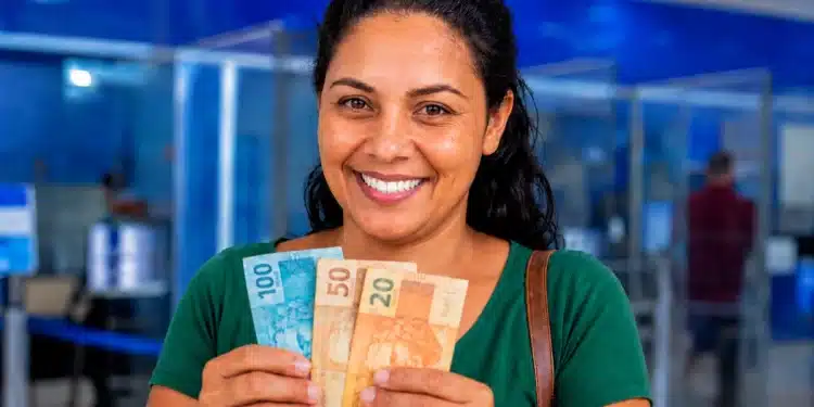 Mulher segurando cédulas em agência bancária, representando o calendário de pagamentos e os adicionais do Bolsa Família em junho de 2026.