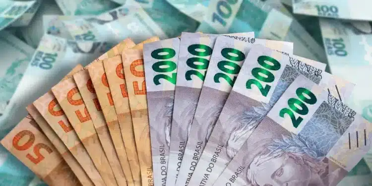Notas de dinheiro real brasileiro sendo seguradas, com notas de R$ 100 ao fundo, ilustrando os depósitos de até R$ 2.625 da Caixa Econômica Federal.