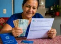 Beneficiária do INSS segura dinheiro e extrato de pagamento, representando a devolução de valores por descontos indevidos.