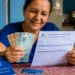 Beneficiária do INSS segura dinheiro e extrato de pagamento, representando a devolução de valores por descontos indevidos.