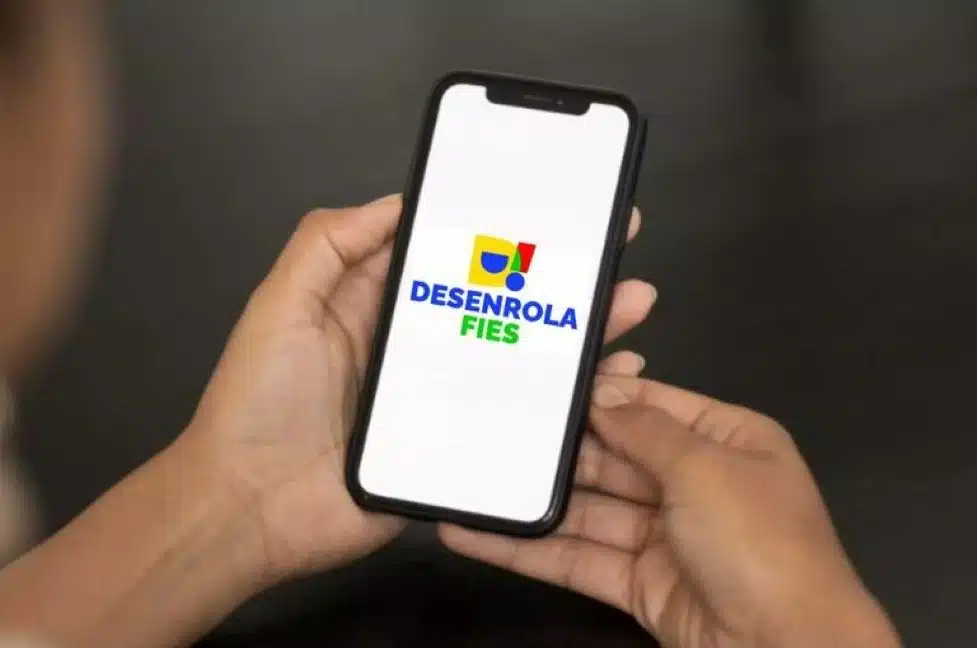 Desenrola Fies 2026 - Renegociações de dívidas estudantis Mãos segurando smartphone exibindo o aplicativo Desenrola Fies, relacionado à renegociação de dívidas estudantis no Brasil.