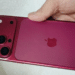 Mão segurando iPhone na cor vinho/burgundy com módulo de câmera tripla e logo da Apple visível.